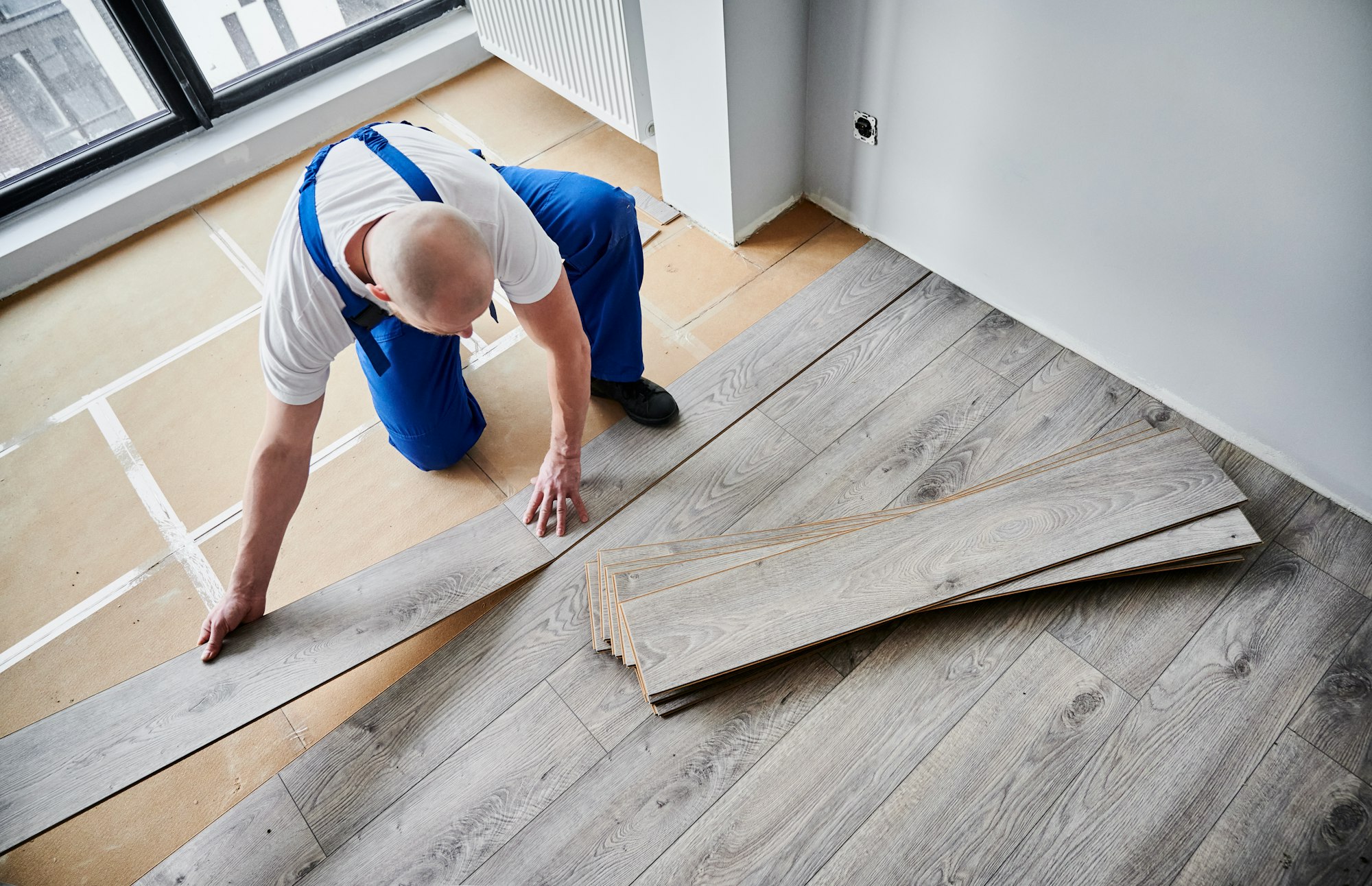 Man installing laminate wood flooring in apartment under renovation.